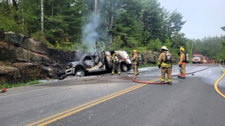 Burned pickup truck, firefighters with hoses, roadside scene