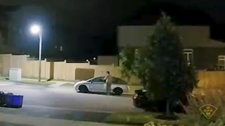Police officer examining a blue car in a residential area at night.