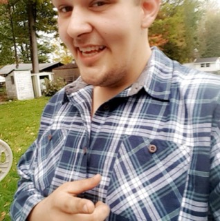 Smiling man in a blue and white plaid shirt, pointing at the camera