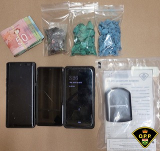 Canadian fifty-dollar bills, small baggies of pills, a smartphone displaying the time, a respirator mask, OPP logo