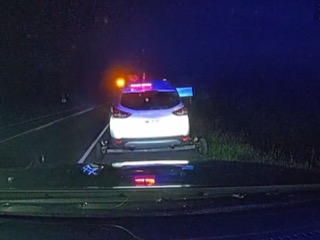 Damaged white SUV with flashing emergency lights. Debris on the road.