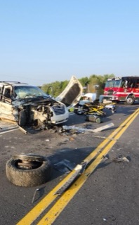 Damaged white pickup truck, debris on road, fire truck in background