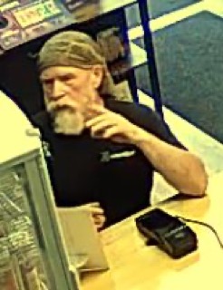 Man with gray beard and headband, looking down and gesturing with his hand.