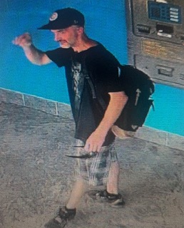 Man wearing a black cap and t-shirt, gray shorts, and a black backpack, skateboarding.