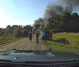 Smoke rising from a distant field, four people standing on a dirt road
