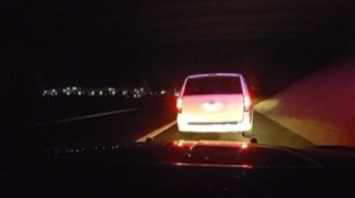 White SUV driving on a dark road, taillights illuminated
