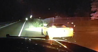 White car headlights illuminate a dark road.