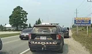 Police SUV with visible damage, parked on the shoulder of a road, other vehicles nearby, roadside sign reads &quot;50 km/h Over Limit Max. Fine = $10 000 Roadside Suspension&quot;
