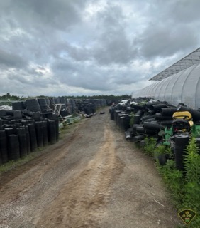Stacked black pots and green planters fill a greenhouse aisle.
