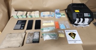 Stacks of Canadian money, small baggies, blue pills, a digital scale, and a money counter on a table.