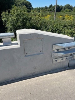 Gray concrete bridge railing with metal plates.