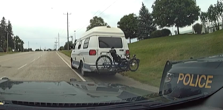 White van with bike rack and bicycles. Police vehicle windshield in foreground.