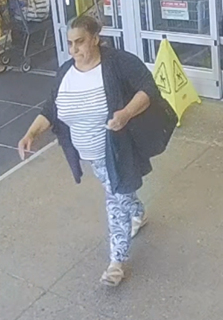Woman walking, wearing a striped shirt, patterned leggings, and a black cardigan, carrying a black bag.
