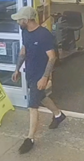 Man in a blue t-shirt and dark shorts, wearing a baseball cap, facing away.