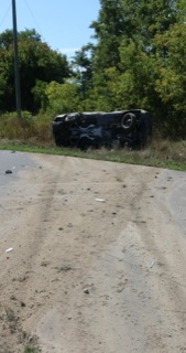 Black car overturned on its roof in tall grass.