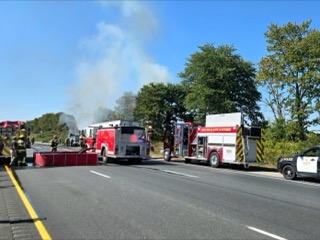 Fire trucks and a police car on a highway, smoke in the background.