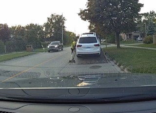 A person in a green uniform working on a utility pole between two SUVs.