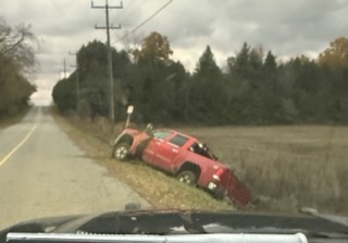 Red pickup truck overturned in a grassy field.