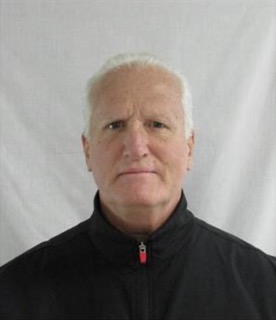 Man with short white hair, black jacket, neutral expression