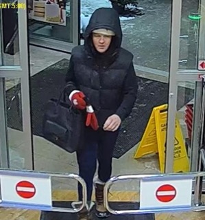 Person in a black hooded coat and dark leggings exiting a building.