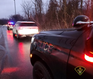 Police cruiser, front view, with visible &quot;POLICE&quot; lettering. Red and blue lights reflected on wet pavement. Another vehicle further back on the road.