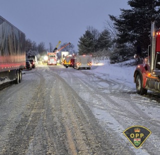 Snow-covered road with emergency vehicles and a truck.