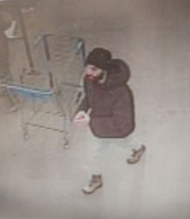 Person in a dark coat and hat, standing near pipes