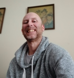 Smiling man with a shaved head, gray hoodie, white t-shirt