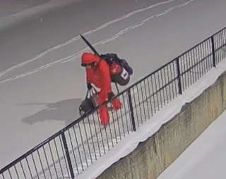Person in red jacket and backpack walking on a snowy bridge.
