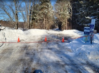 Snow-covered road blocked by traffic cones and a red rope.