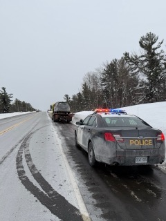 Police car with &quot;POLICE&quot; in large letters, snow-covered road, tow truck in distance