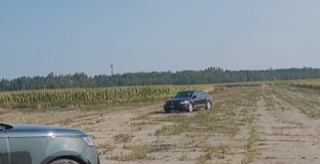 Black car on a dirt road, green field and trees in background