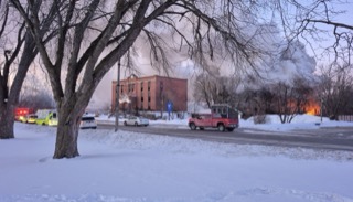 Snow-covered street with emergency vehicles and a brick building.