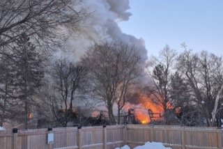 Large fire with thick smoke and flames visible above trees.