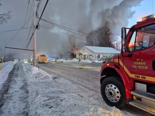 Fire truck with snow-covered ground and smoke in the background.