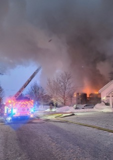 Fire truck with extended ladder, snow-covered yard, orange flames visible through windows, dark sky