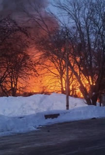 Orange and red sunset behind bare trees and snow-covered ground