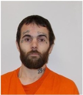 Man with a dark beard and neck tattoos, wearing an orange jumpsuit.