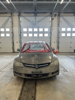 Silver Acura with front end damage, covered in plastic sheeting and red tape.