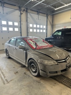 Damaged gray sedan with a red tarp covering the hood and windshield
