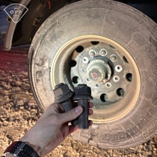 Two lug nuts in a hand, blurry tire in background