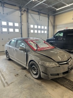 Silver sedan with front-end damage, covered in plastic wrap