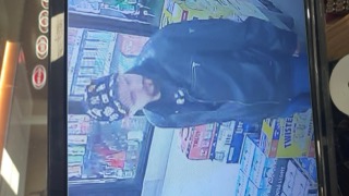 Man in a dark hoodie looking down. Beer cans visible in the background.