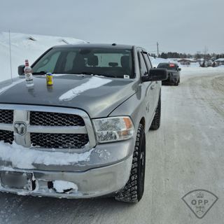 Gray pickup truck covered in snow, windshield partially obstructed, snow-covered road, OPP vehicle in background