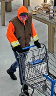 Person pushing a shopping cart, wearing an orange hoodie, brown vest, and black gloves