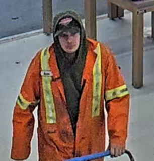 Person in orange work jacket and hood, holding a blue tool