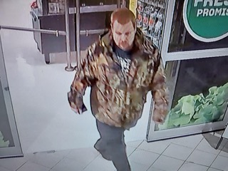 Man in a distressed brown jacket and gray pants, walking toward the viewer.