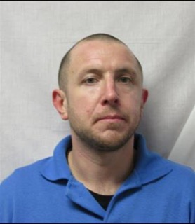 Man with a shaved head wearing a blue polo shirt