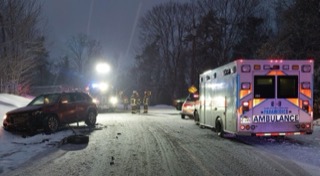 Damaged red SUV in snow, emergency responders and ambulance on scene