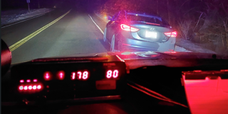 Dashboard display showing 80 in a 70 mph zone. Red and brake lights of a car ahead.